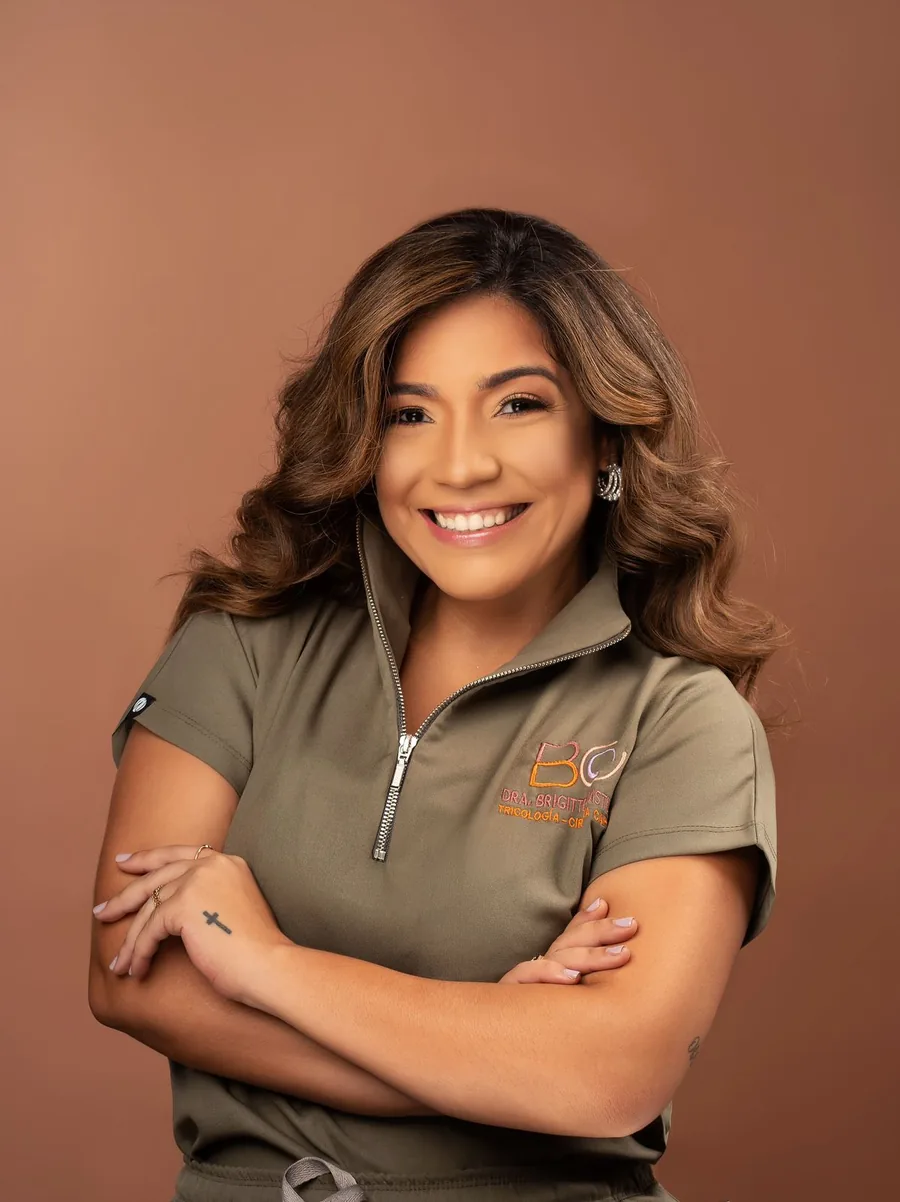 La Dra. Brigitte Castillo sonríe a cámara con los brazos cruzados; lleva su uniforme verde oliva con el logo BC bordado